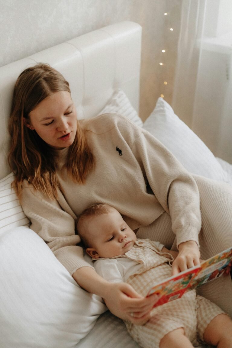 Woman reading a colorful book to her baby while lying on a cozy bed indoors.